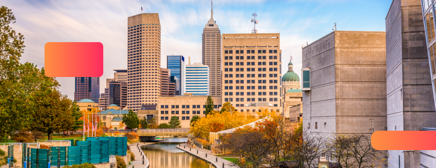 Downtown Indianapolis skyline with tall modern buildings, the Indiana Statehouse dome visible, and the canal walk lined with autumn trees in the foreground under a bright sky with light clouds. Orange and pink gradient design elements overlay parts of the image.Using online notary service NotaryLive with a notary public near me.